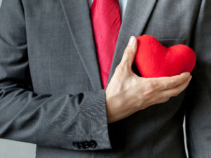 Businessman showing compassion holding red heart onto his chest in his suit - crm service mind business concept.