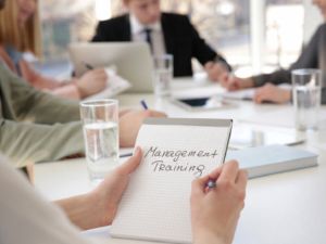 Woman holding notebook with text MANAGEMENT TRAINING at business presentation